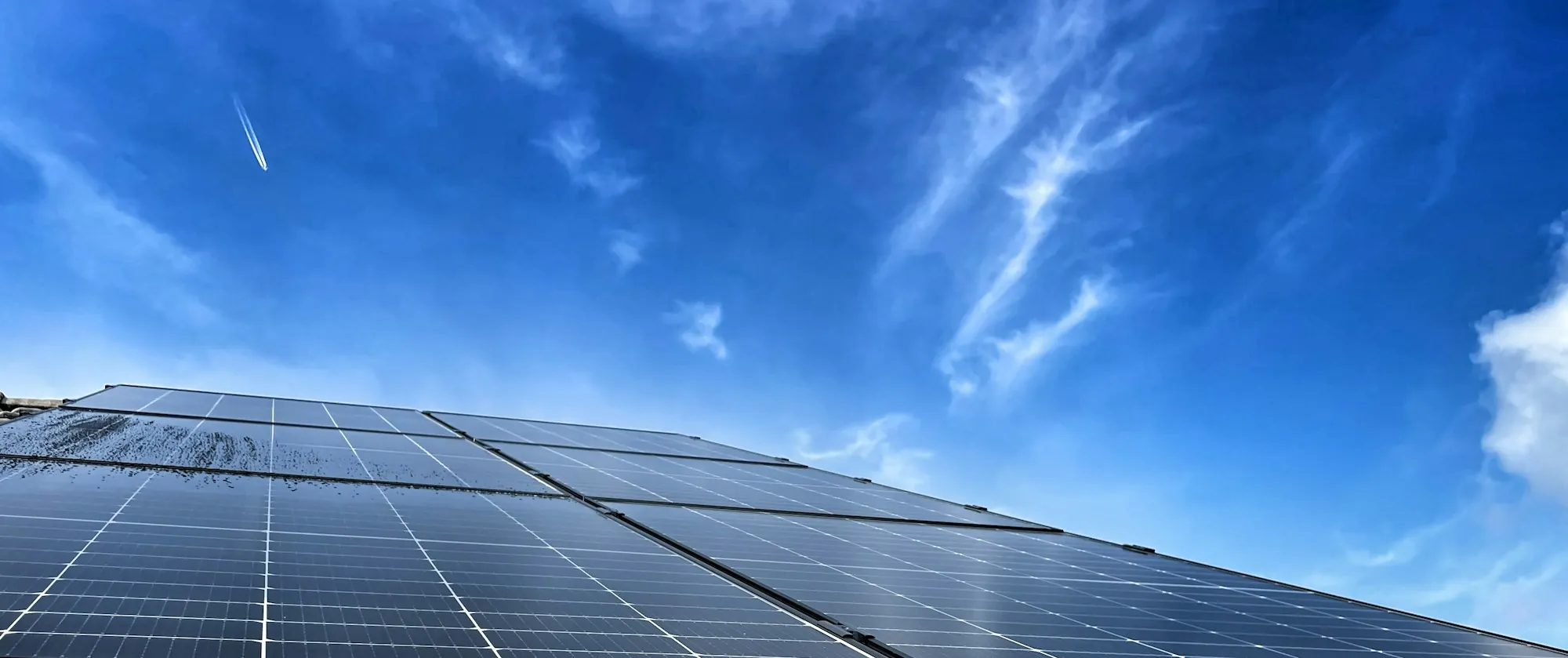 Rooftop solar panels angled against a bright blue sky with wispy clouds