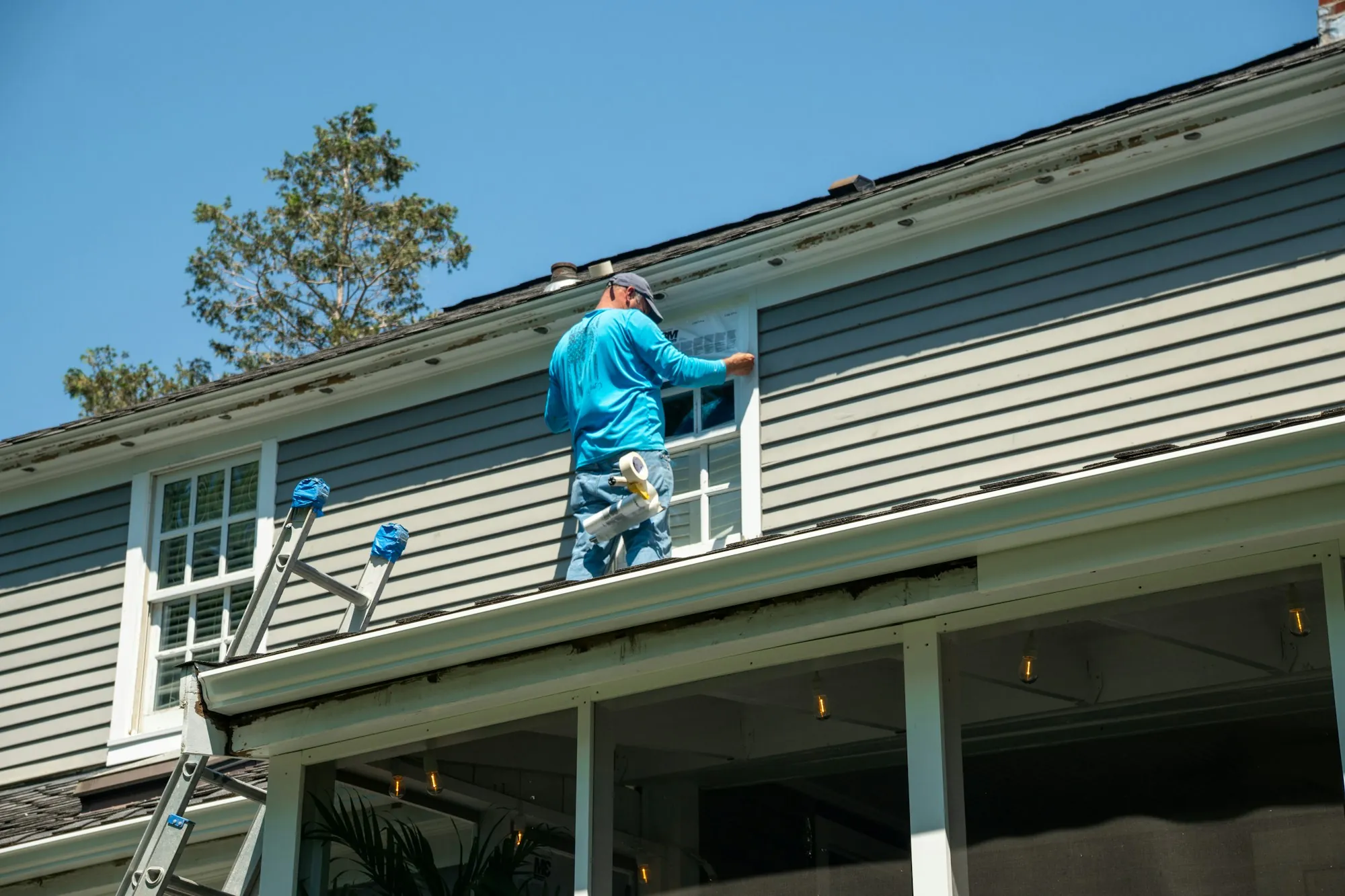 Worker standing on a porch roof beside the siding of a two-story house