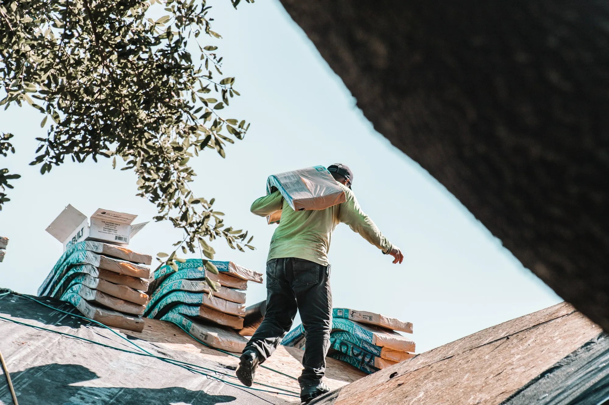 Roofer carrying a bundle of shingles across a roof with stacked shingle packs, the stage after a solar detach before tear-off in Chicago Ridge